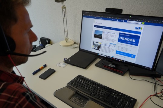 Ein Mann sitzt vor einem Monitor und demonstriert die Sprachsteuerung per Headset.