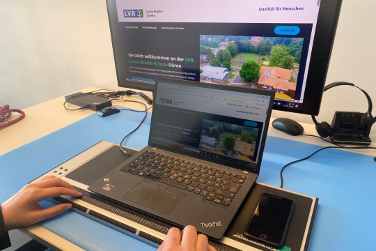 Laptop mit Braillezeile sowie ein Monitor auf der die Webseite der LVR-Louis-Braille-Schule ist