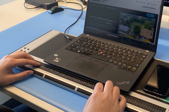 Zwei Hände an einer Braille-Tastatur bedienen ein Laptop.