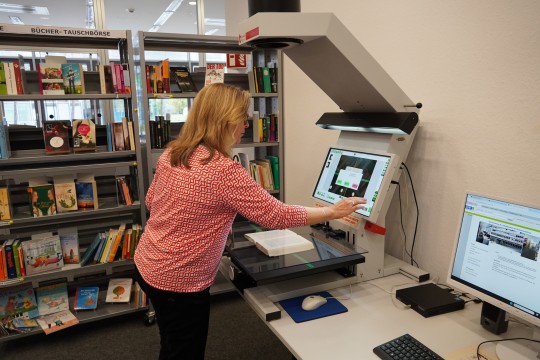 Eine Frau bedient den Scanner in der LVR-Bibliothek. Im Hintergrund ist ein Bücherregal.