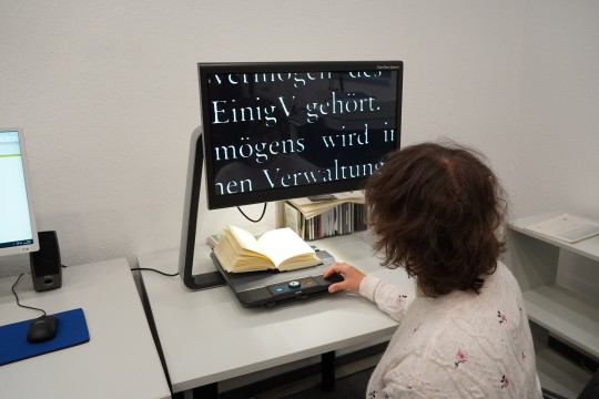 Eine Frau vor einem Bildschirmlesegerät mit stark vergrößertem Buchtext.