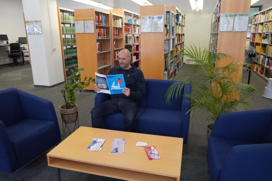 Ein Mann liest eine Zeitschrift in einer Sitzgruppe im Lesesaal der Bibliothek.